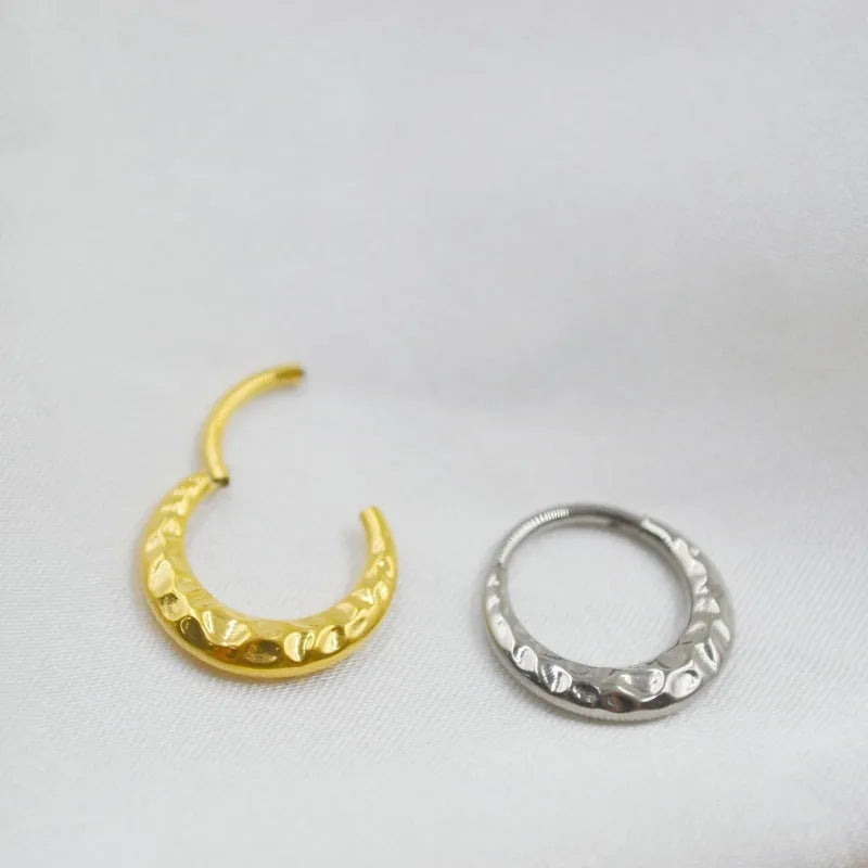 Close-up of a concave-convex titanium nose ring in gold finish on a grey background.