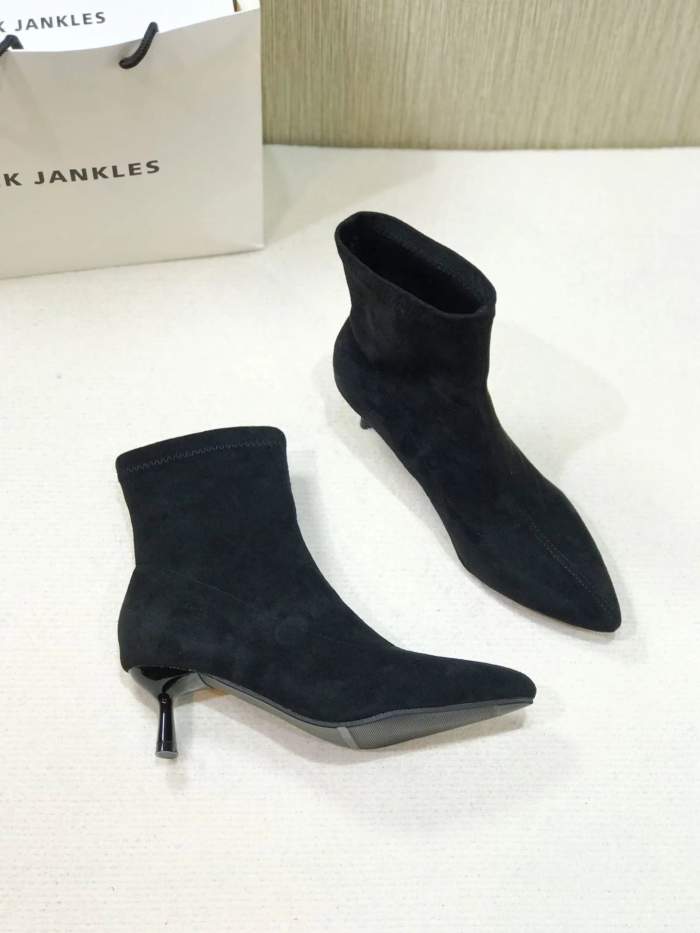 Black pointed toe women's ankle boots with a stiletto heel on a plain background.