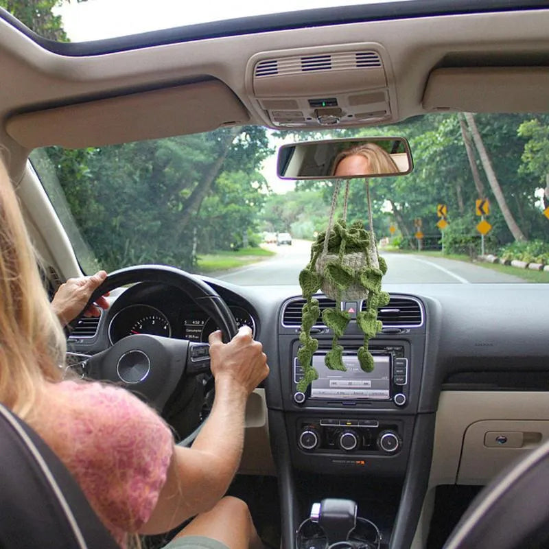 Green and white knitted wool car plant decoration with hanging rope on a car dashboard