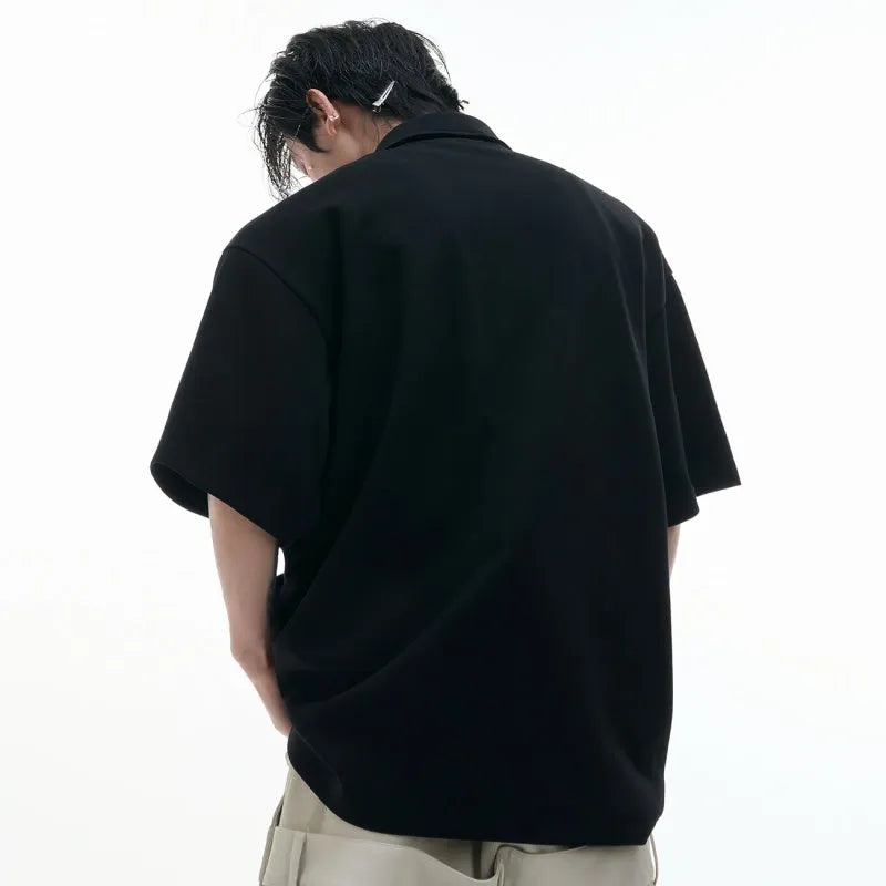 Man modelling a loose-fit black polo shirt with a deconstructed collar and a geometric pattern on the chest.