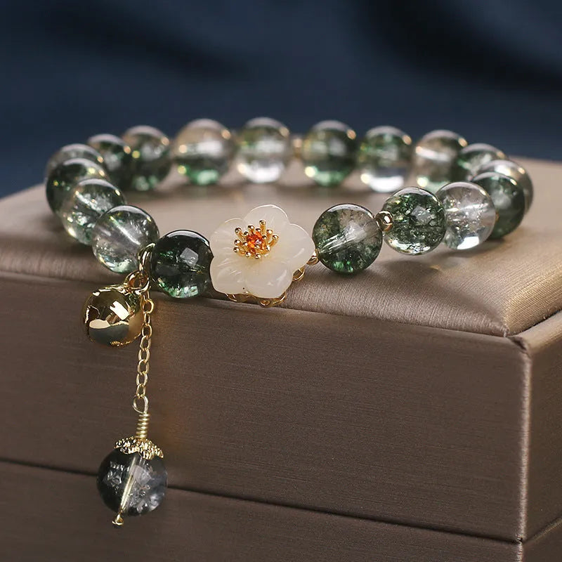 Green Phantom quartz crystal bracelet with white jade flower on a plain background