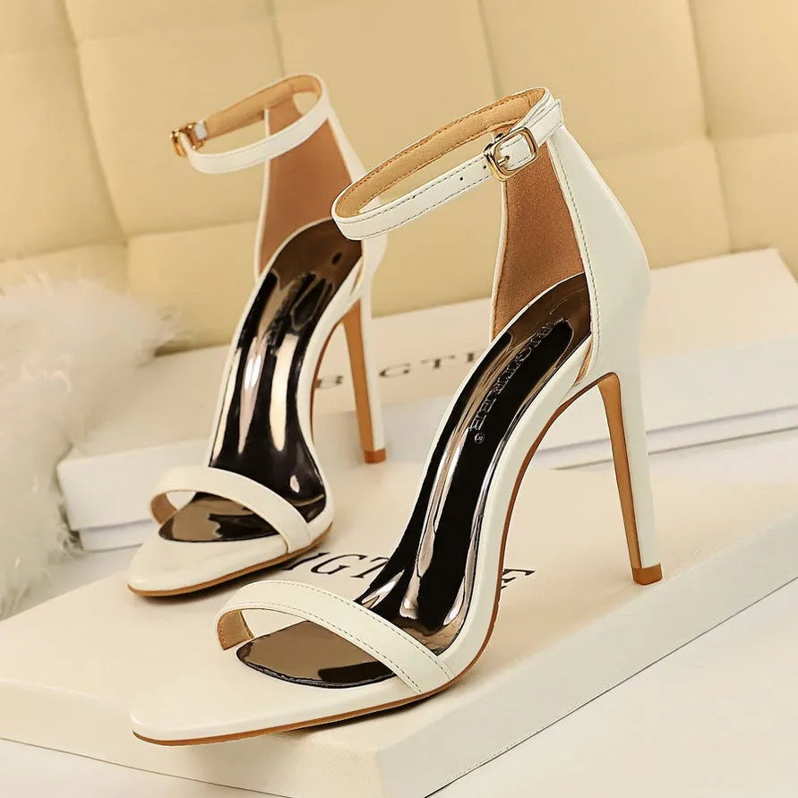 Women's white open-toe high heel sandals with an ankle buckle strap on a plain background.
