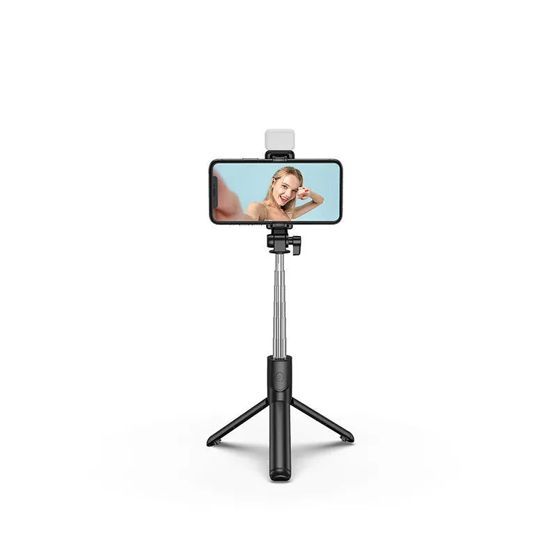 Black Bluetooth selfie stick with extended tripod legs, fill light, and a phone mounted in the 360-degree rotatable holder.