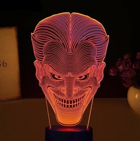 A 3D acrylic LED lamp showing a gradient of colours, sitting on its square base with a remote control nearby.