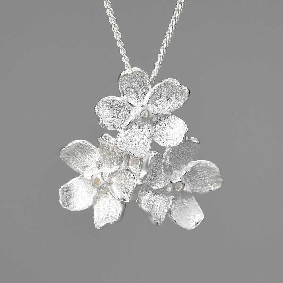 Silver open mouth Myosotis Sylvatica flower pendant with electroplated finish on a dark background.