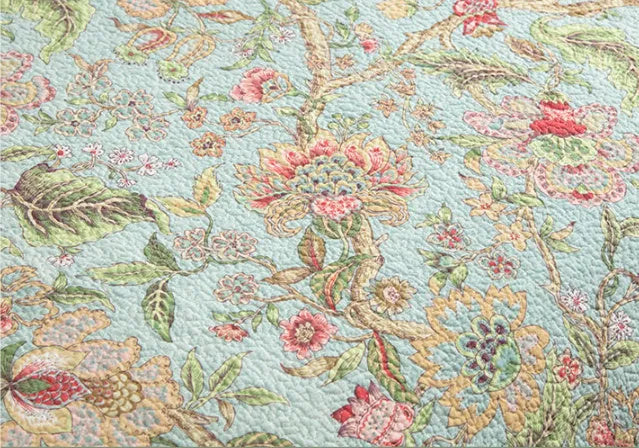 Blue American floral and bird pattern quilted cotton bedspread set of three pieces on a bed.