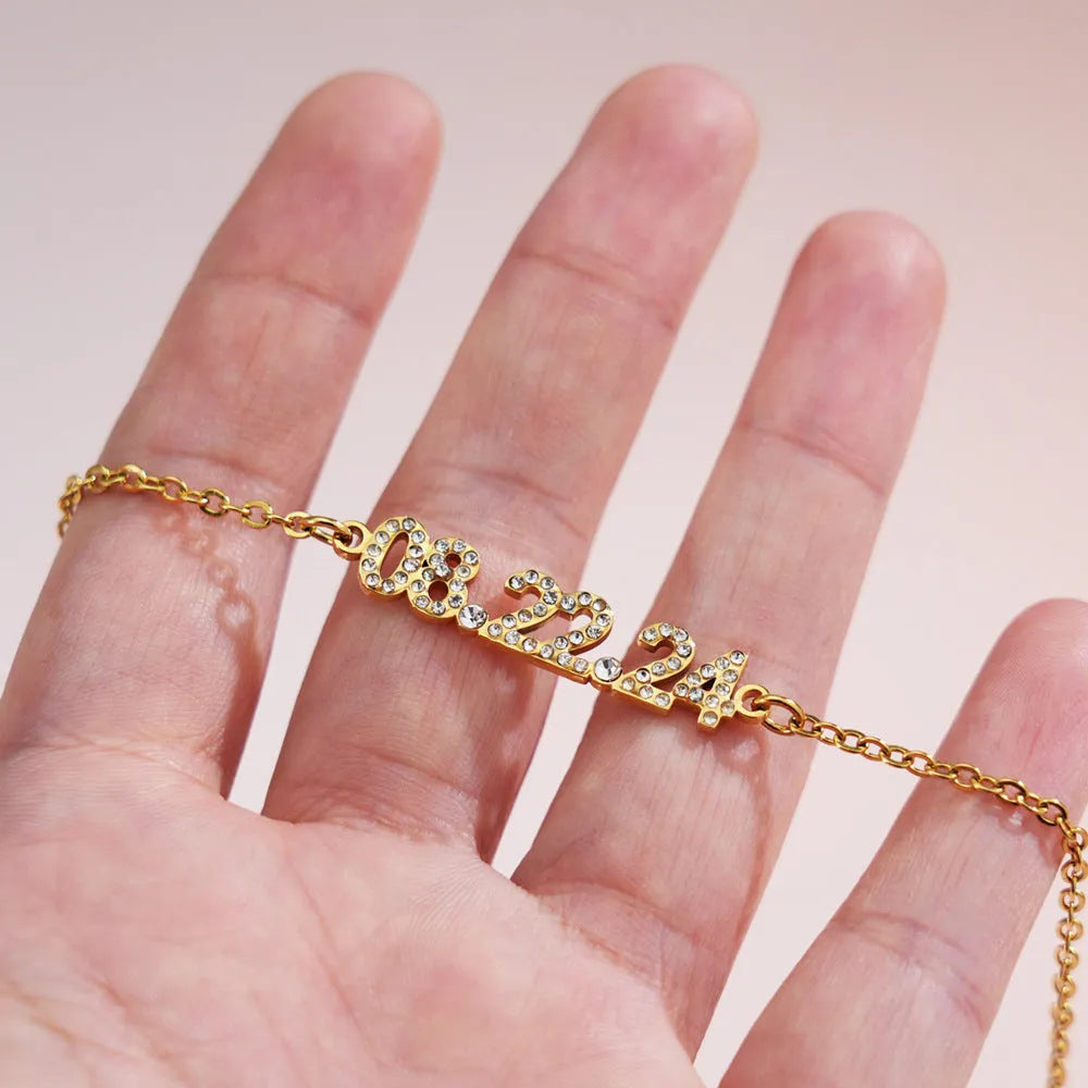 Stainless steel digital bracelet or necklace with diamond-set numbers on display, shown in gold colour.
