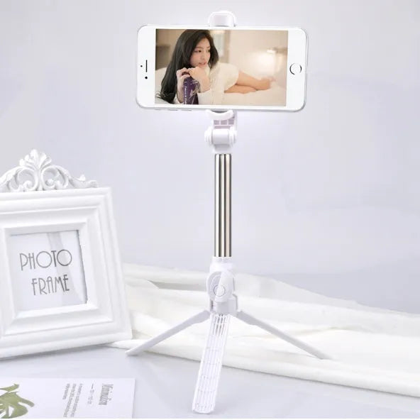 Black Bluetooth selfie tripod with extended stand and 360-degree rotating phone clip attached to an iPhone.