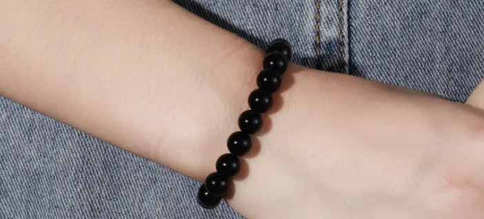 Close-up of a women's geometric bracelet with black agate beads on a black elastic cord.