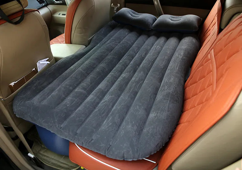 Black inflatable car bed with flocked material and two pillows, set up in a car's rear seats.