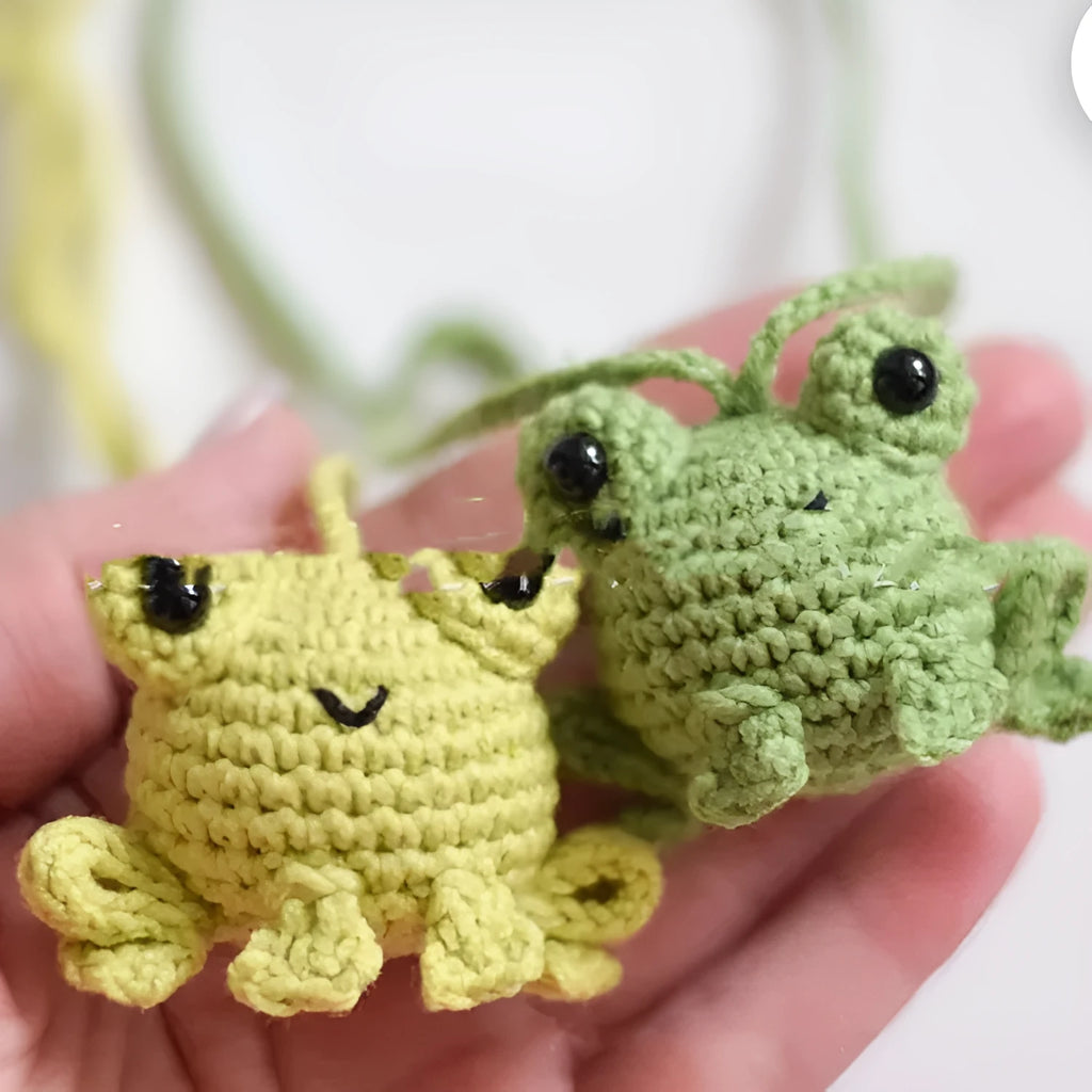 Handmade woven green plush frog car pendant hanging from a rear-view mirror.