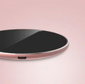 Ultra-thin aluminum wireless charger in silver on a desk next to a phone.