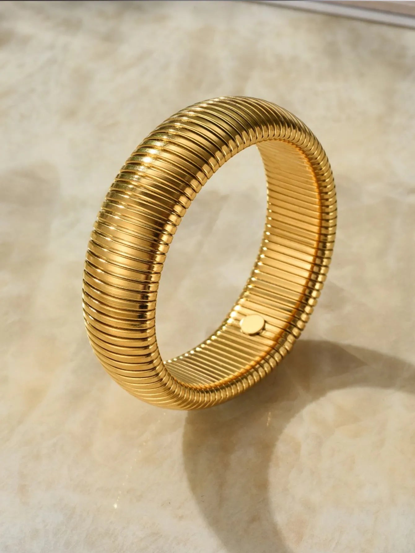 Close-up of a women's titanium steel bracelet with a vertical stripe ring pattern, shown in a gold tone finish on a wrist.