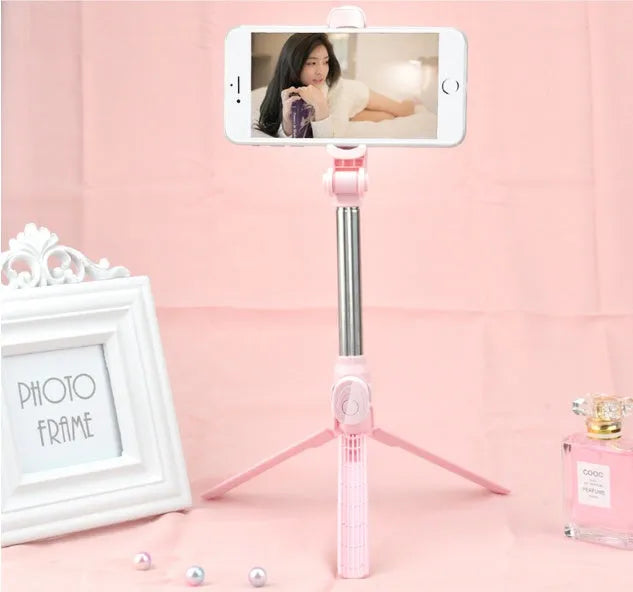 Black Bluetooth selfie tripod with extended stand and 360-degree rotating phone clip attached to an iPhone.