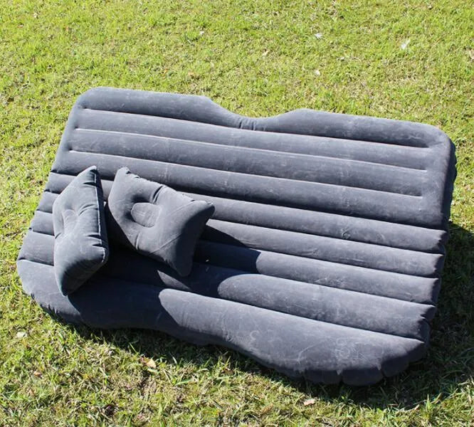 Black inflatable car bed with flocked material and two pillows, set up in a car's rear seats.