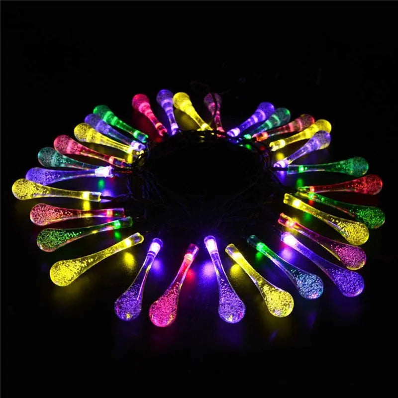 Solar-powered LED outdoor string lights with bubble drop pendants decorating a garden fence