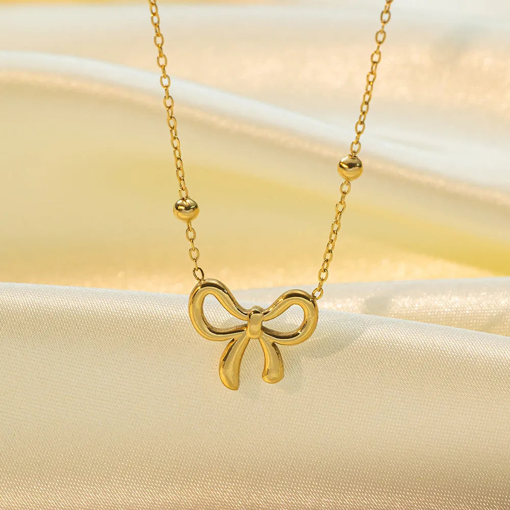 Gold electroplated bow design necklace with cross chain on white background