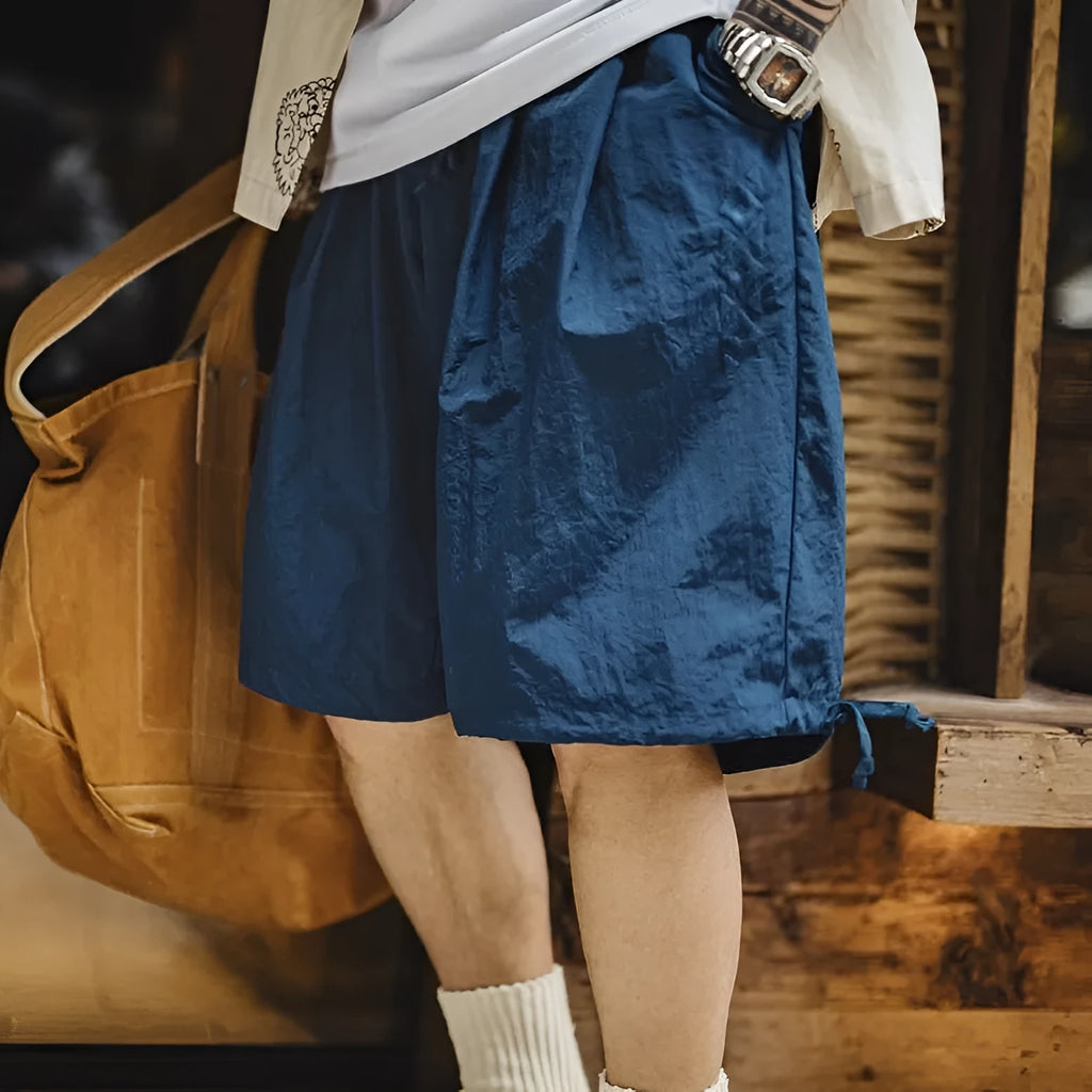 Prussian blue men's loose fit nylon shorts with embroidery on a plain background.