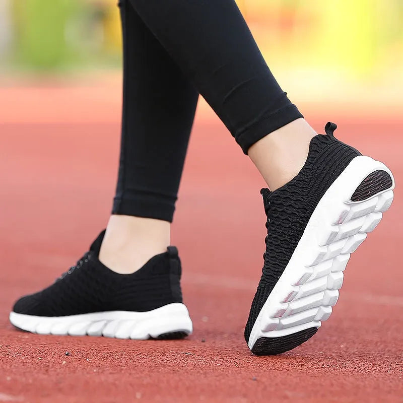 Women's running shoes in black, pink, or white with a woven fly knit upper and textured outsole.