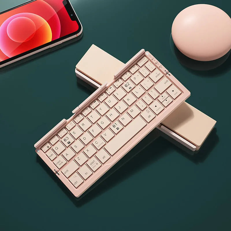 Silver white folding Bluetooth keyboard open next to a smartphone on its built-in metal stand.