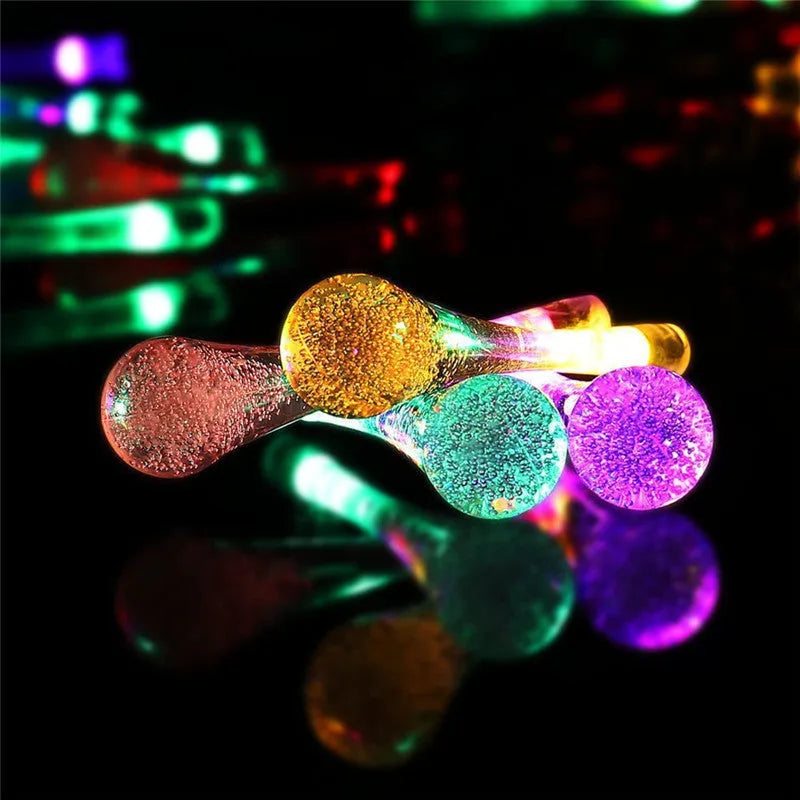 Solar-powered LED outdoor string lights with bubble drop pendants decorating a garden fence
