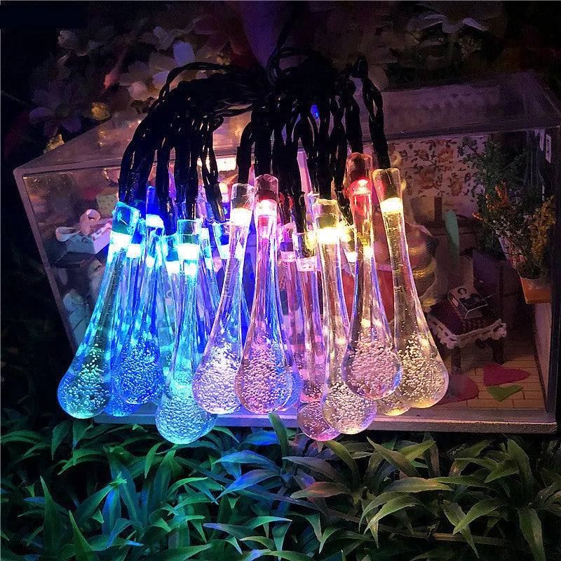 Solar-powered LED outdoor string lights with bubble drop pendants decorating a garden fence