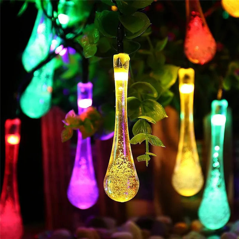 Solar-powered LED outdoor string lights with bubble drop pendants decorating a garden fence