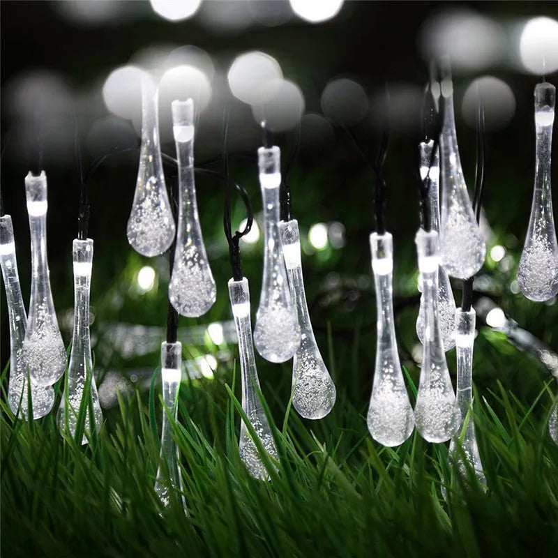 Solar-powered LED outdoor string lights with bubble drop pendants decorating a garden fence