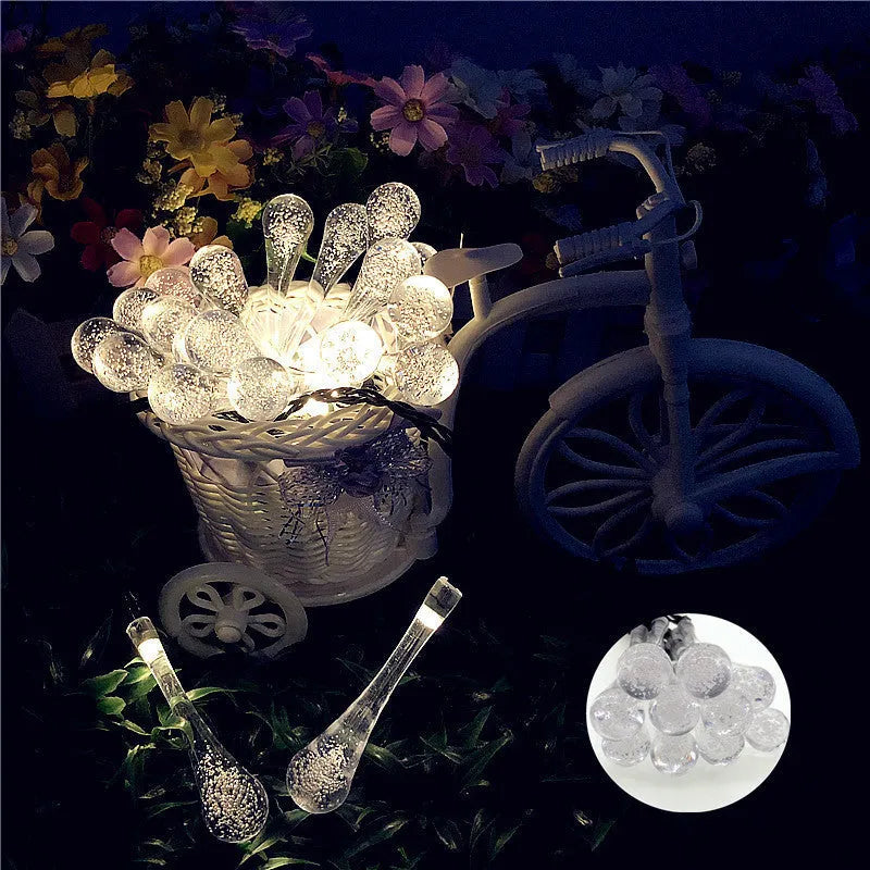 Solar-powered LED outdoor string lights with bubble drop pendants decorating a garden fence