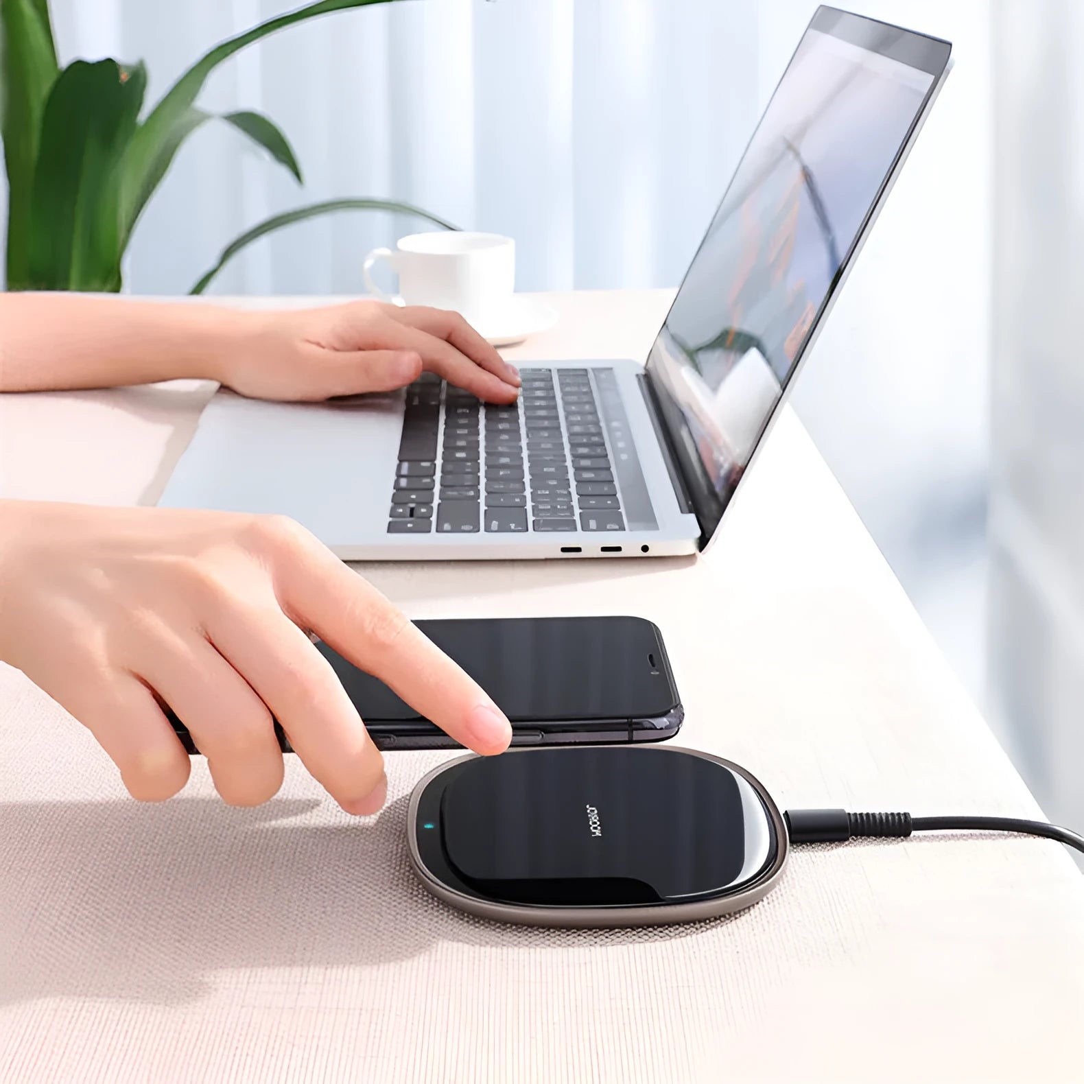 Black 15W wireless fast charger with zinc alloy frame and glass top on a wooden desk.