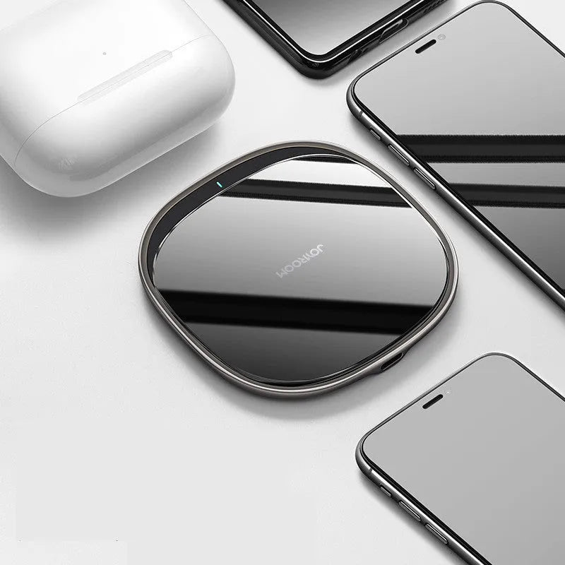 Black 15W wireless fast charger with zinc alloy frame and glass top on a wooden desk.