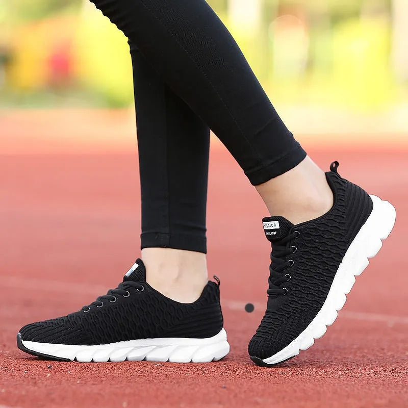 Women's running shoes in black, pink, or white with a woven fly knit upper and textured outsole.