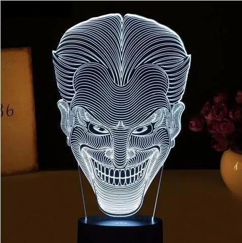 A 3D acrylic LED lamp showing a gradient of colours, sitting on its square base with a remote control nearby.