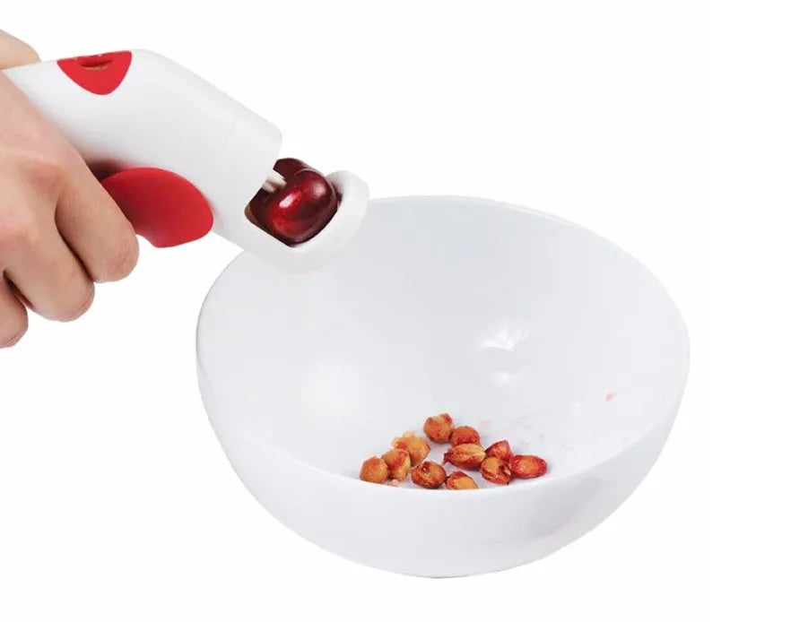 Manual handheld cherry kernel remover kitchen gadget with stainless steel blades and clear pit catcher.