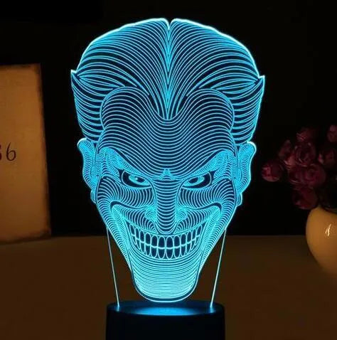A 3D acrylic LED lamp showing a gradient of colours, sitting on its square base with a remote control nearby.