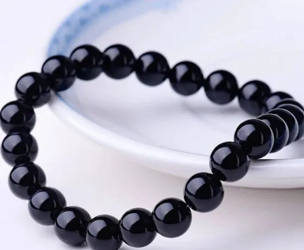 Close-up of a women's geometric bracelet with black agate beads on a black elastic cord.