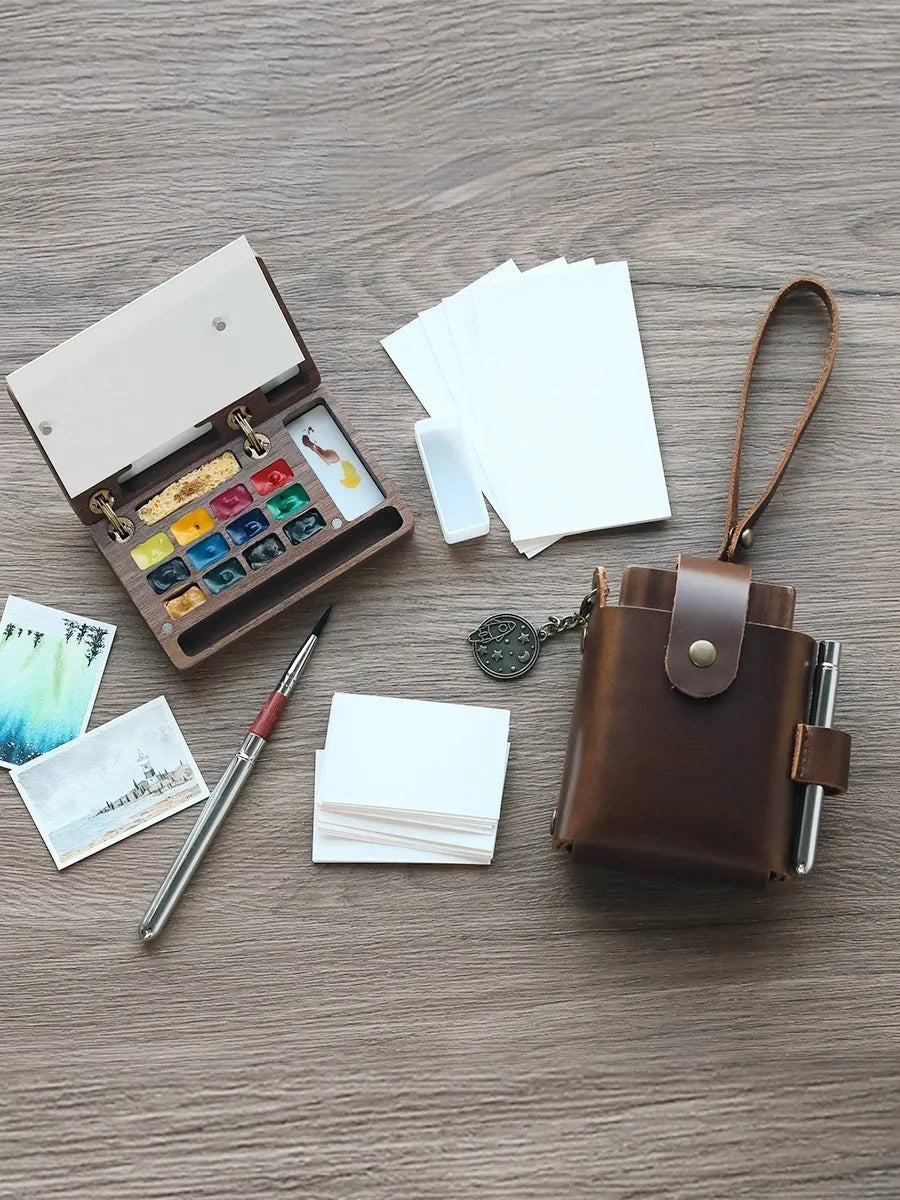 Mini walnut wood watercolour paint box open to show pigment pans with leather carrying bag