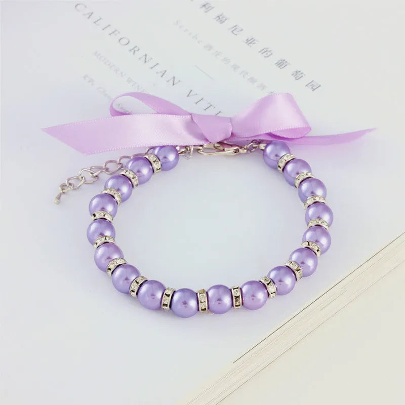 Small dog wearing adjustable pearl and rhinestone necklace with soft ribbon bow in blue colour