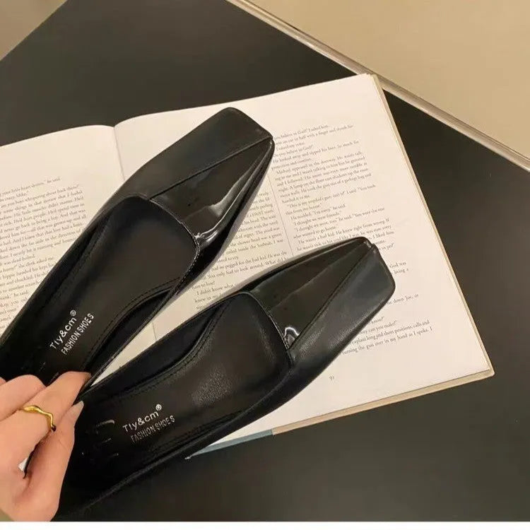 Women's low heel square toe retro pumps in black PU leather with short chunky heel, side view on light background