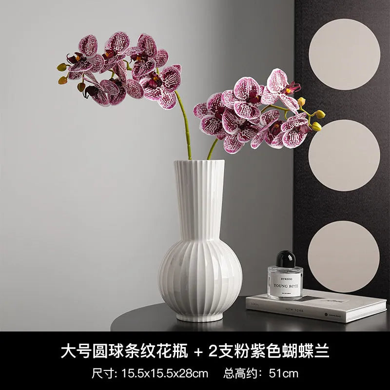 White ceramic ball vase with blue stripes and artificial blue orchid flowers on a wooden table.