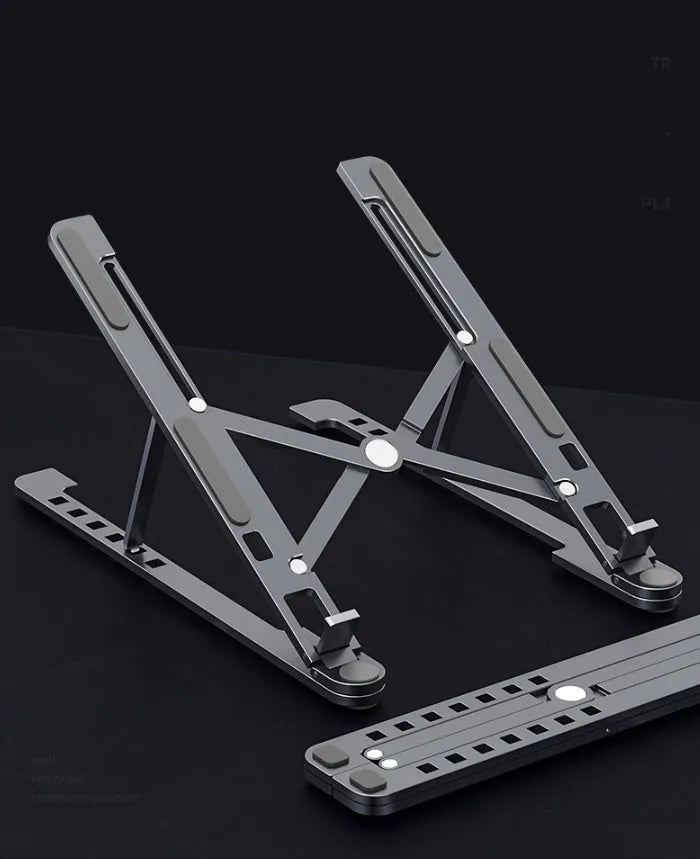 Deep grey portable aluminium laptop stand, folded flat next to an open laptop showing its adjustable height.
