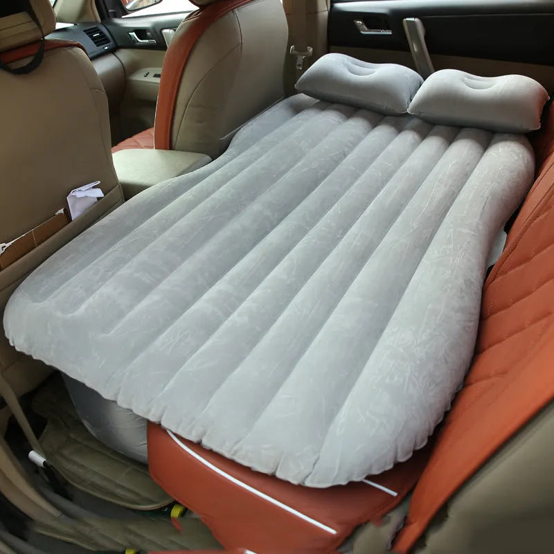 Black inflatable car bed with flocked material and two pillows, set up in a car's rear seats.