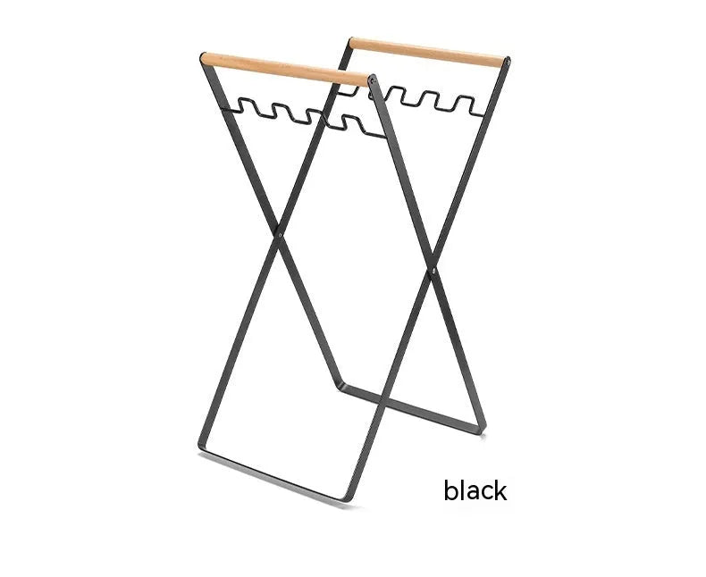 Folding black outdoor trash bag hanger with wooden carry handle on a patio.
