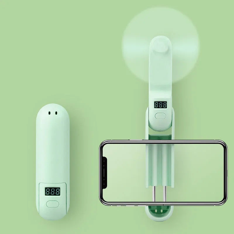 Green folding mini fan with plastic blades open, showing USB charging port.