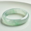 Light green jade bracelet showing natural stone texture with sizing chart displaying 53mm to 64mm circumference options