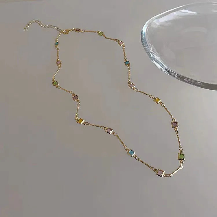 Square geometric clavicle chain necklace in gold tone with artificial crystal details on a model.