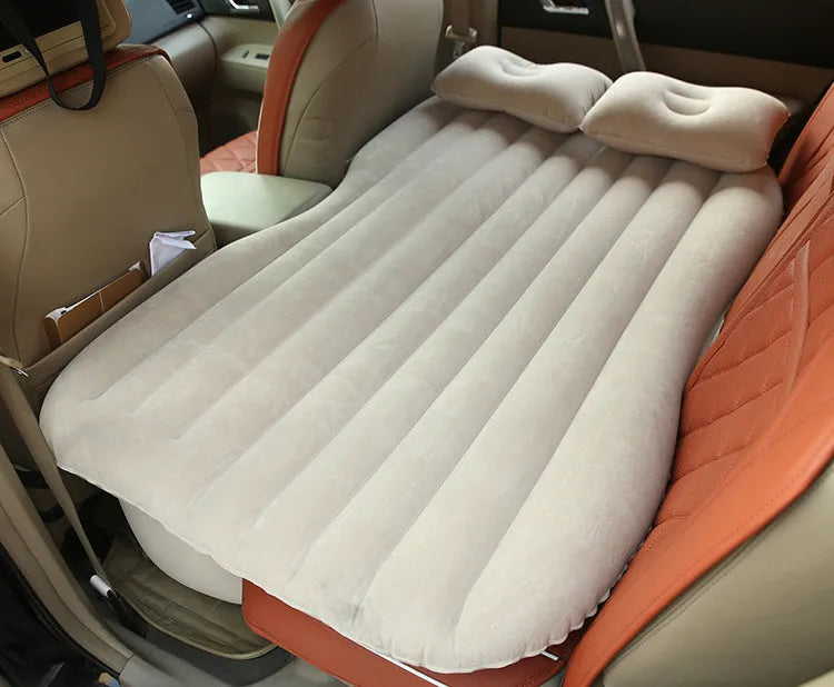 Black inflatable car bed with flocked material and two pillows, set up in a car's rear seats.