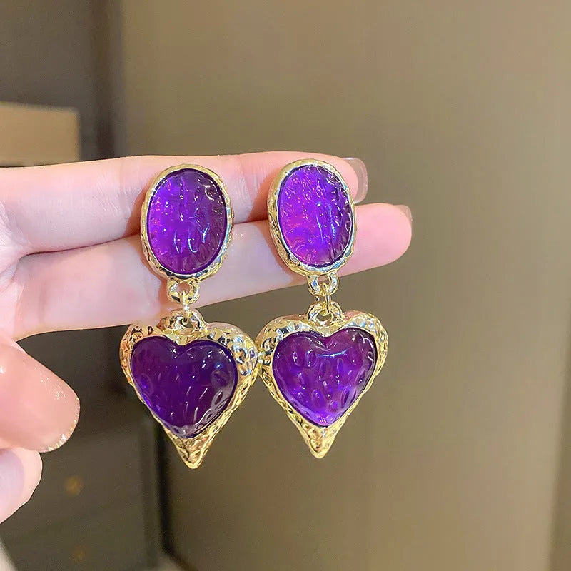 A pair of oval-shaped, pleated love heart stud earrings in alloy, shown in various colours.