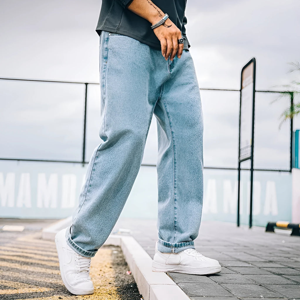 Man wearing dark blue loose straight-cut cotton jeans with a mid-waist and zipper fly.