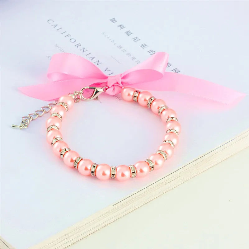 Small dog wearing adjustable pearl and rhinestone necklace with soft ribbon bow in blue colour